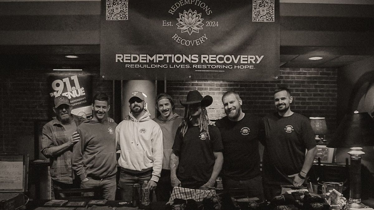Redemptions Recovery team standing together under the house banner at a community event.
